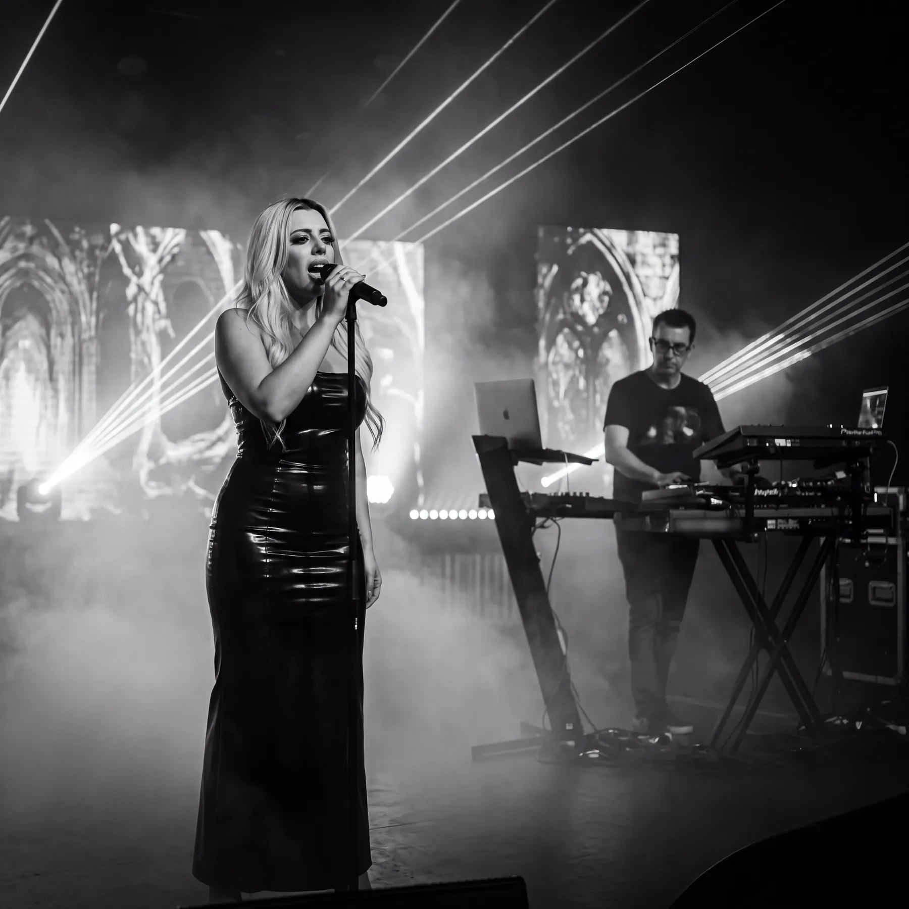 Kat singing at a microphone stand with gothic cathedral visuals on the screens behind her
